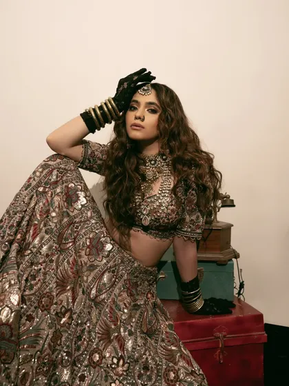 This shot incorporates vintage luggage as a prop, building on the theme of a bride's journey. The model's pose is both strong and elegant, showcasing the full lehenga.