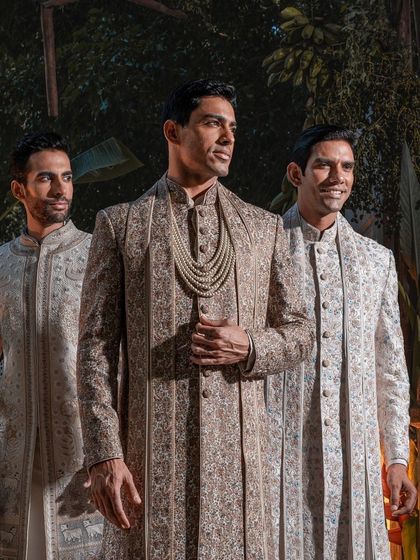 The groom and his entourage, captured in a moment of shared celebration. This image highlights our coordinated wedding ensembles, where the groom's layered sherwani is complemented by the elegant attire of his groomsmen.