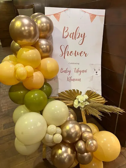 A stylish welcome sign for the baby shower, decorated with a matching earthy-toned balloon garland and dried palm leaves.