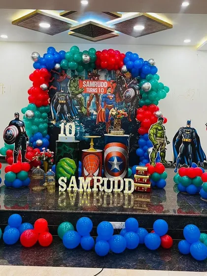 This is an action-packed Avengers theme party I designed for a 10th birthday. The stage features a custom backdrop with all the major superheroes, character cutouts of Batman, Superman, and Iron Man, and balloon columns in the classic red, blue, and green superhero colors.
