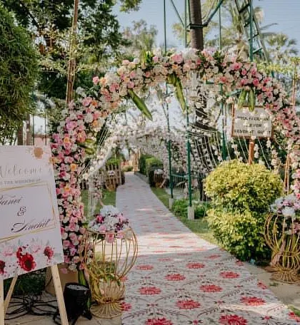 A romantic floral archway serves as the entrance to this beautiful garden wedding. The custom welcome sign and patterned aisle runner add personalized touches to the classic design.