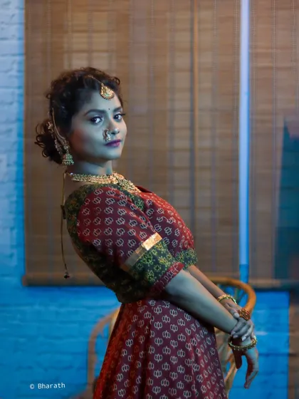 A side-profile portrait in a traditional red and green printed outfit. The lighting and pose create a classic, painting-like quality, perfect for showcasing heritage jewelry.
