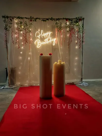 Even a simple setup can be stunning. Here, we used a sheer curtain with fairy lights, a 'Happy Birthday' neon sign, and a red carpet to create an elegant and affordable party corner.