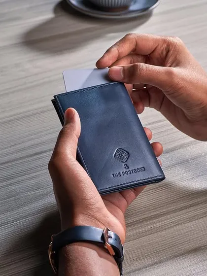 A close-up, in-use shot of a leather wallet from The Postbox. This image focuses on the utility of the product, showing how a card slides in, and captures the feel of a quiet coffee shop moment.