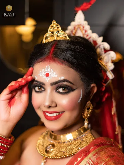 A classic Bengali bridal look. The signature elements are the bold, kohl-rimmed eyes, the red bindi with white चंदन designs, and the radiant smile. It’s a look full of tradition and joy.