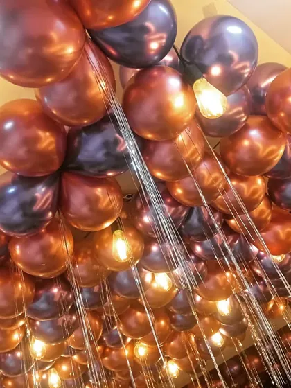 A close-up shot of metallic balloons on a ceiling, mixed with hanging light bulbs. This is a great way to add ambiance to a restaurant or bar party.