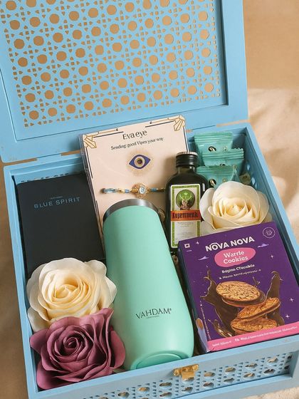 A modern and stylish Rakhi box for your brother. This hamper includes a Vahdam tumbler, Zara perfume, an evil eye rakhi, a Jägermeister miniature, and delicious waffle cookies.
