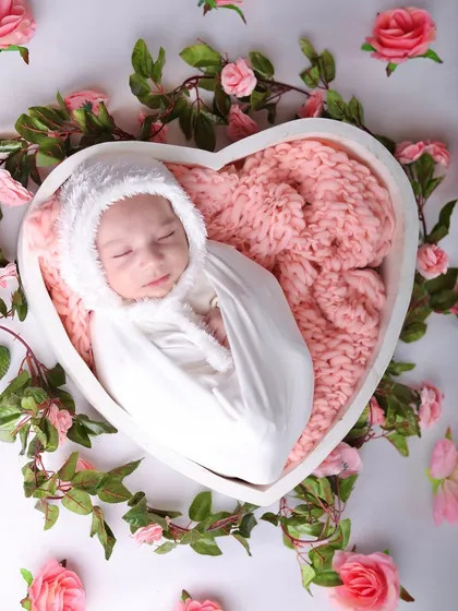 A romantic and sweet setup with a baby in a heart-shaped bowl, surrounded by a wreath of pink roses.