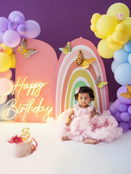 A full portrait of the birthday girl in her gorgeous pink dress, seated in front of the elaborate balloon and butterfly decorations.