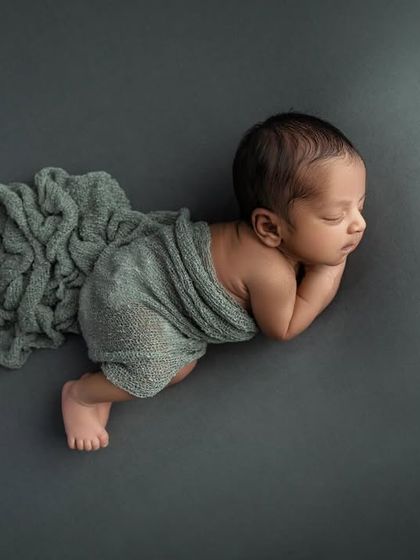 An artistic overhead shot of a baby in a side pose, with a grey wrap elegantly draped. This composition creates a sense of movement and grace.