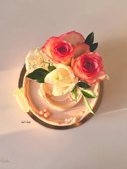 A blush pink buttercream cake adorned with fresh pink and white roses and baby's breath. The soft colors and floral arrangement make it perfect for romantic occasions.