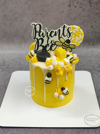 A cheerful "Parents to Bee" baby shower cake. This bright yellow cake is decorated with cute bees, macarons, and a honeycomb-patterned lollipop.