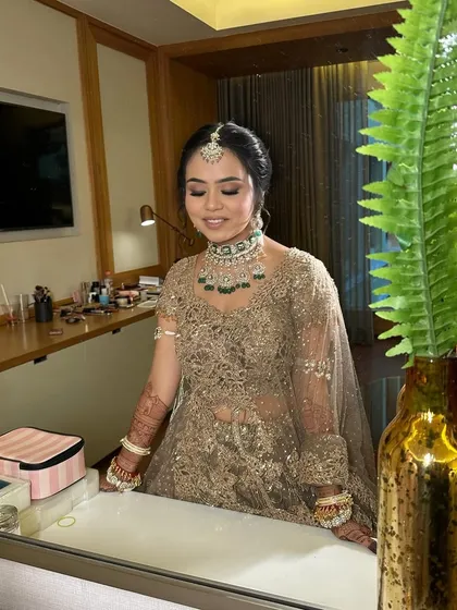 Riya admiring her final bridal look in the mirror. The soft lighting highlights her glowing skin and the intricate details of her makeup and hair.