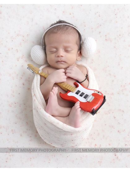 A future rockstar. This classic swaddled pose is made fun with the addition of a miniature guitar and headphones, showing that simple setups can also be creative.
