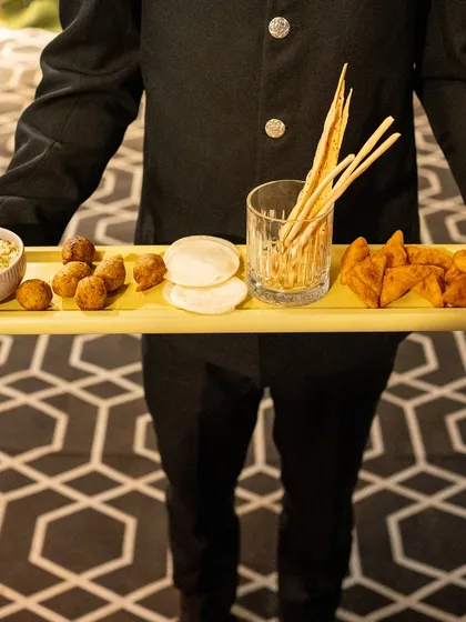 A server holds a tray laden with a variety of our savoury bites, including arancini, samosas, and breadsticks, showcasing the breadth of our appetizer menu.