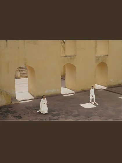 An architectural wide shot in Jaipur, where the couple stands apart yet connected by the space. This artistic composition uses shadows and light to create a dramatic effect.