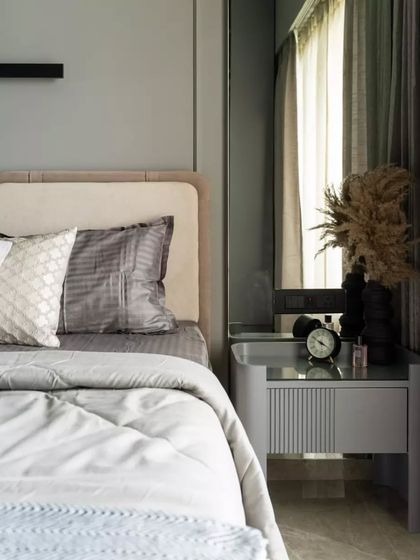 This bedroom design effortlessly combines modern elegance with serene functionality. The soft beige upholstered headboard adds a touch of warmth and comfort, harmonizing perfectly with the muted gray walls to create a calming ambiance.