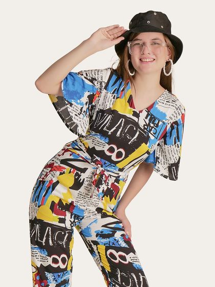 A fun and energetic pose from a model wearing a colorful, newspaper-print jumpsuit, perfect for a brand with a bold personality.