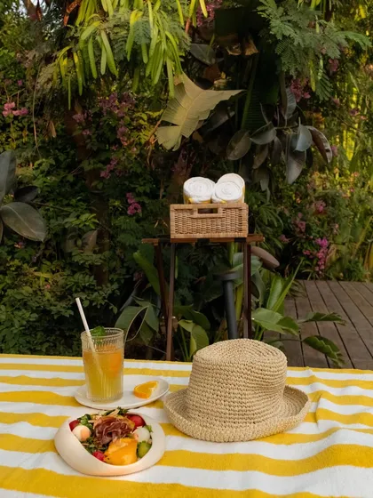A poolside scene ready for relaxation, with a fresh salad, a cool drink, and a woven sun hat.