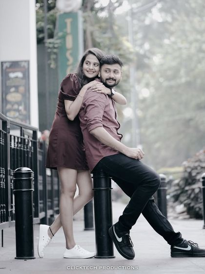 A stylish pose on a city sidewalk, with the bride hugging the groom from behind as he sits on a bollard.