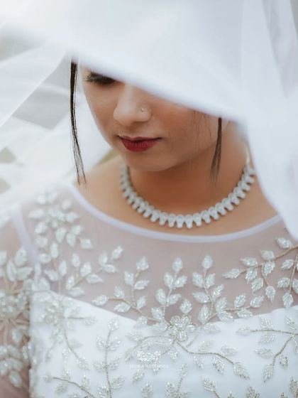 A close-up portrait of the bride through her veil, focusing on the delicate details of her gown's neckline and her jewelry.