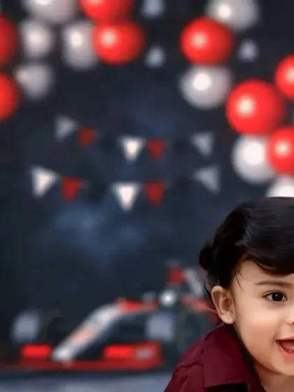 A happy baby's face peeks into the frame, with a race car themed party backdrop blurred in the background.