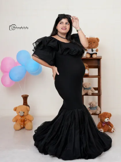 A fun and stylish studio portrait in a black mermaid-style gown. The setup includes teddy bears and gender-reveal colored balloons.