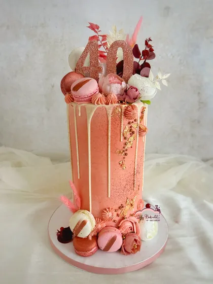 This extra-tall rose gold drip cake was for a fabulous 40th anniversary. I layered it with macarons, fresh florals, and a touch of gold leaf to create a sophisticated and celebratory dessert.