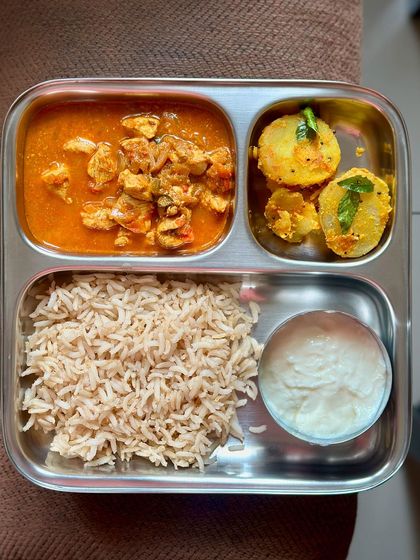 A comforting meal of brown rice with chicken curry, sautéed potato, and a side of curd.