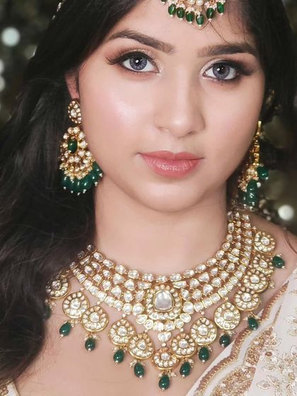 An elegant bride in a white saree, wearing a multi-layered Kundan necklace with green bead drops. A timeless and classic look.