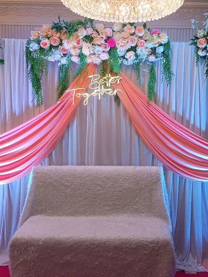 For this engagement, we used soft peach drapes and lush floral arrangements on the top and sides. The setup is illuminated with spotlights to highlight the stage area in a banquet hall.