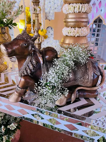 An ornate brass Nandi statue, decorated with baby's breath flowers, used as a prop in a traditional baby shower setup.