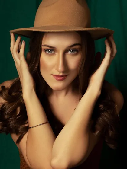 A classic portrait with a fedora hat, giving it a cool, bohemian vibe. The dark green background makes the warm tones of the outfit pop.