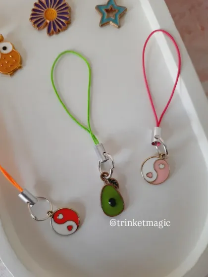 A close-up of the avocado and yin-yang phone charms. These quirky and meaningful charms are perfect for personalizing your phone.