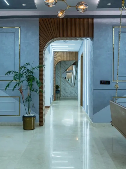 A wider view of the SNN Clermont entryway, showing the interplay of the blue walls with gold trim, the wooden arch, and the dramatic linear lighting.