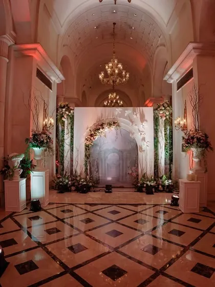 A wide shot of the grand entryway, showcasing the symmetrical design with floral-adorned pedestals, classical statues, and a central archway leading into the main event.