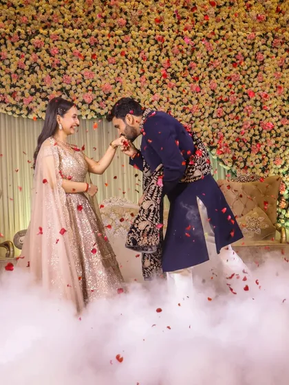 A dynamic shot of the groom kissing his fiancée's hand amidst a shower of rose petals, capturing the movement and romance of the moment.