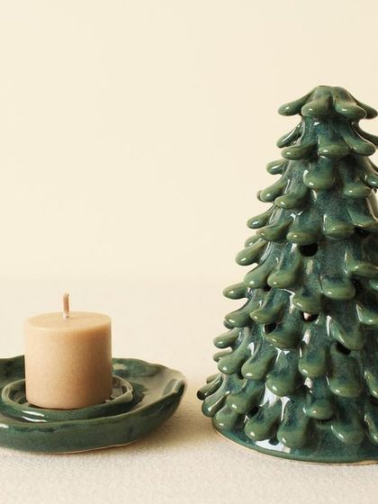 The Coniferous Christmas tree luminary next to a small candle. Once lit, the light flickers through the individually attached clay leaves, creating a magical effect.