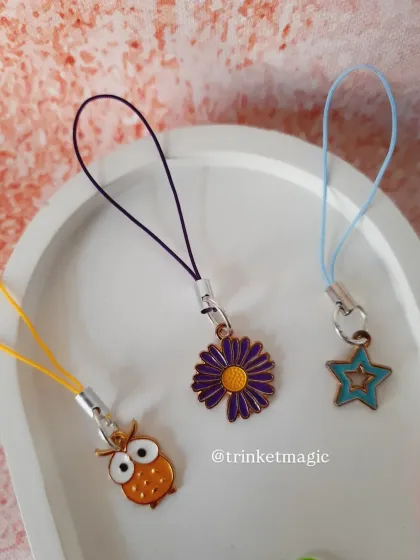 A close-up of the owl, daisy, and star phone charms. Each one is attached to a colorful cord, ready to add personality to your tech.