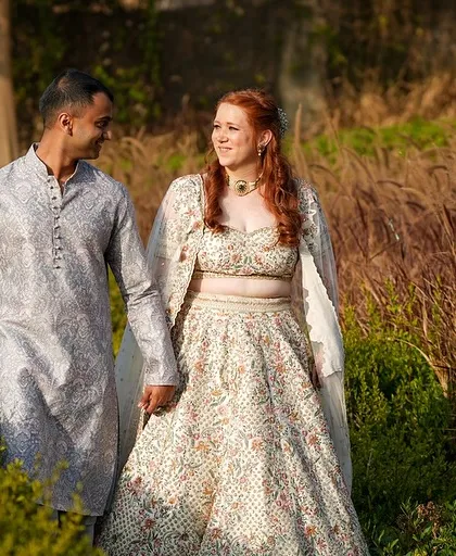 A happy couple walking through the gardens of Alila Fort, their modern yet traditional outfits blending perfectly with the surroundings.