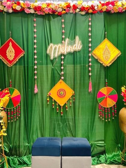 A simple yet striking Mehndi backdrop. I used a rich green drape with colorful traditional hangings and a 'Mehndi' neon sign for a modern, minimalist vibe.
