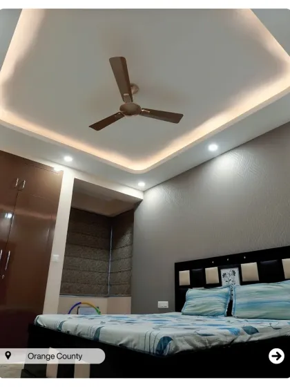 Another bedroom in Orange County, this one with a dark grey accent wall and a simple, modern bed. The false ceiling with cove lighting adds a soft glow.
