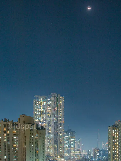 A rare celestial alignment of Jupiter, Venus, and the crescent Moon is captured in the night sky above Mumbai's city lights.