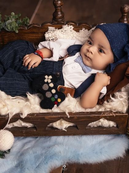 Game on! This awake and alert baby is ready for some fun, holding a tiny game controller in a detailed, playful setup complete with a miniature bed.