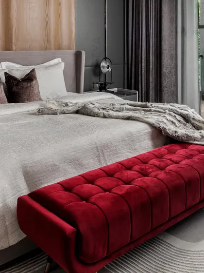 A close-up on the rich, tufted red velvet ottoman, which provides a powerful color contrast against the neutral bedding and grey rug. It’s a perfect example of using a single piece to add personality.