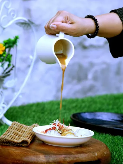 Experience the culinary master's touch. A rich, flavorful broth is poured over a bowl of noodles and garnishes, showcasing an interactive and elegant serving style.