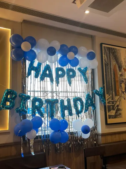 A simple and classic birthday decoration in blue and white. The foil 'Happy Birthday' letters are paired with balloon flowers against a window with a shimmer curtain.