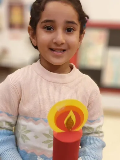 A close-up of a smiling student and her beautifully crafted Christmas candle. The sparkle and bright colors really capture the festive spirit.