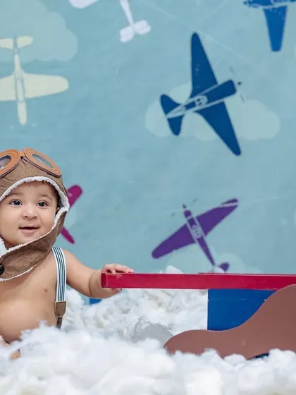 This sitter session features a little pilot in an aviator hat, sitting among fluffy clouds with a toy plane, against a backdrop of vintage aircraft.