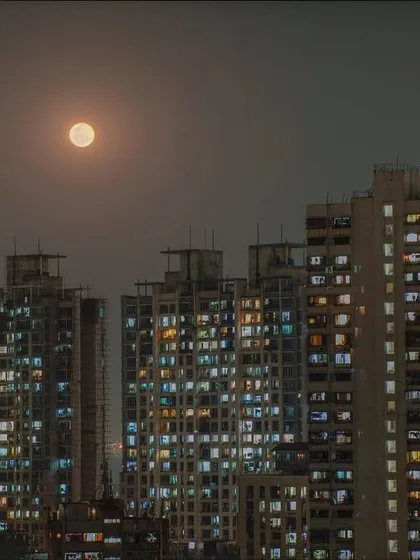 A full moon glows through the haze above a dense cluster of residential buildings in Mumbai at night.